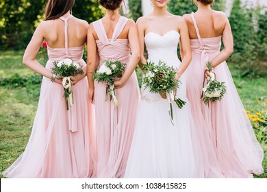 three bridesmaids in powdery dresses transformers with bouquets in hands stand with their backs near the bride in a white dress with a wedding bouquet in her hand on a green lawn