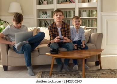 Three Brother Boys Playing Computer Games On A Laptop And Video Games With Joysticks In Their Hands