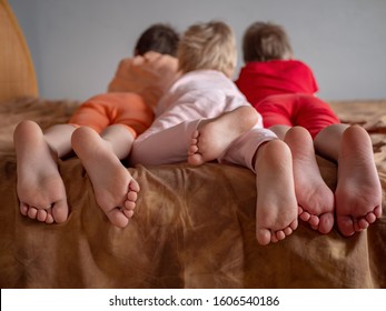 Three Brother Boys Were Lying On Couch And Were Busy With Phone And Tablet. Boys Are Wearing Barefoot Home Pajamas. Feet And Toes Closeup. Tender Baby Feet