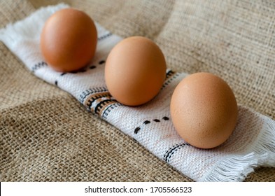 Three Brown Chicken Eggs On Burlap. A Line Of Raw Farm Eggs On A Rushnyk. A Rolled Towel With Eggs On Burlap. Angled Side View. Close-up. Selective Focus.