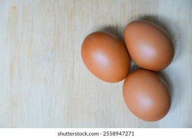 Three brown eggs rest on a wooden surface, highlighting their natural tones and smooth texture. A minimalistic composition representing simplicity and wholesome cooking essentials - Powered by Shutterstock