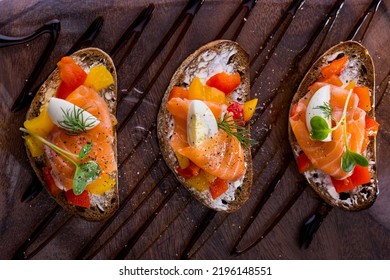 Three Bruschetta With Salmon, Baked Yellow And Red Paprika, Mozzarella And Microgreen Pea Sprouts. Bruschettes Are On A Transparent Plate With Balsamic Sauce.