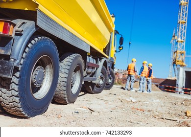 Three Builders In Uniform Standing Near A Big Yellow Tip Truck At Construction Site