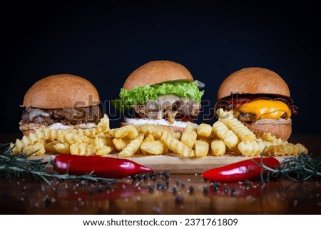 Three burger sliders placed on a wooden board. Very tasty burgers with melted cheese, cheddar, bacon, lettuce, tomato, onion and sauce. Craft beef burgers and french fries, hand made.