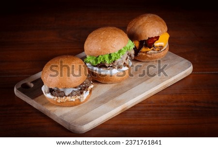 Three burger sliders placed on a wooden board. Very tasty burgers with melted cheese, cheddar, bacon, lettuce, tomato, onion and sauce. Craft beef burgers, hand made.