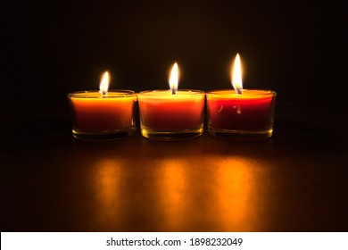 Three burning candles in the dark lighting the table, black background