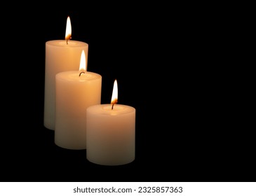 Three burning white candles with different size isolated on black background.
