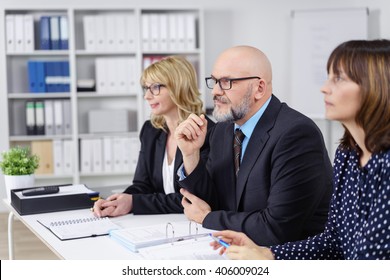 Three business colleagues in a meeting sitting at a conference table in the office listening to a colleague or presentation with concentration - Shutterstock ID 406009024