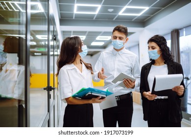 Three business colleagues in protective face mask discussing work related matters on an office building hallway. Teamwork during pandemic in quarantine city. Covid-19.