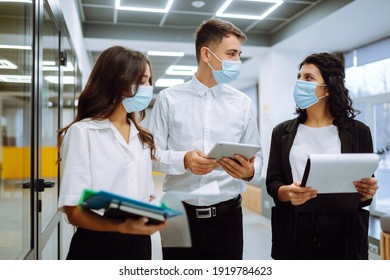 Three business colleagues in protective face mask discussing work related matters on an office building hallway. Teamwork during pandemic in quarantine city. Covid-19. - Powered by Shutterstock