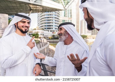 Three Business Men Walking In Dubai Wearing Traditional Emirati Clothes. Different Generation Business People Working Together