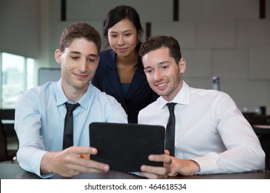 Three Business People Looking At Tablet Computer Screen And Smiling