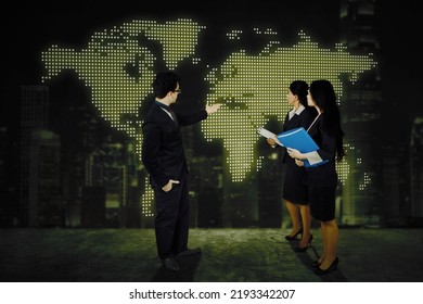 Three Business People Showing World Map In The Virtual Screen While Discussing And Meeting In The Office With