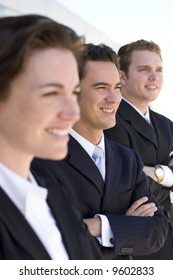 Three Business People Standing In A Row With Arms Folded Looking In The Same Direction