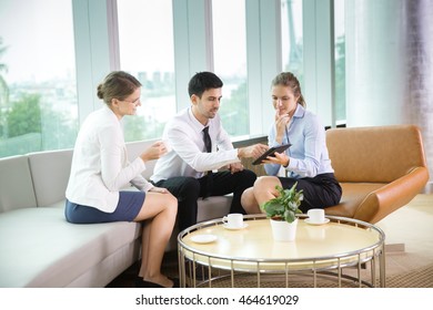 Three Business People Using Tablet PC In Cafe