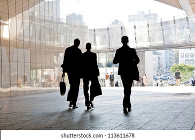 Three Business People Walking Down The Street Talking. Silhouettes. Motion Blur.