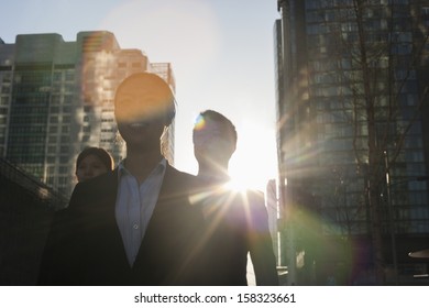 Three Business People Walking Down City Street With Sunlight At Their Back