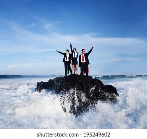 Three Business People Wearing Superhero Costumes Posing On A Rock With Gushing Waves.