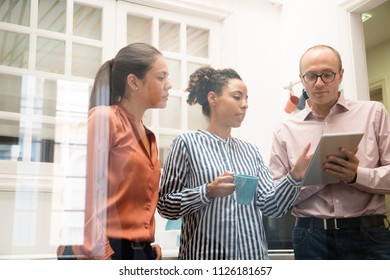 Three Business Team Members Standing In An Office Kitchen And Discussing Content Displayed On A Pc Tablet