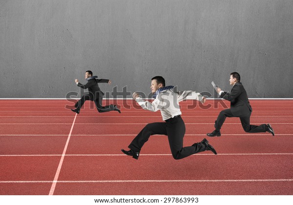 Three businessmen running on red track, with\
gray concrete wall\
background.