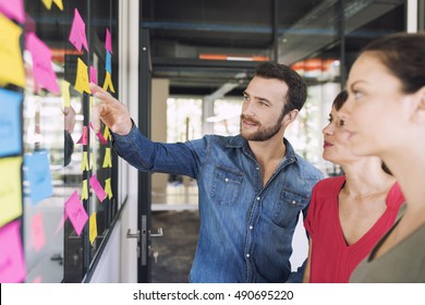 Three businesspeople discussing and planning concept. Front of glass wall marker and stickers. Startup office.