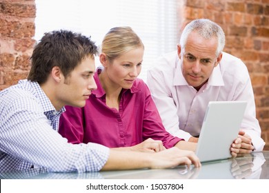 Three Businesspeople In Office Looking At Laptop