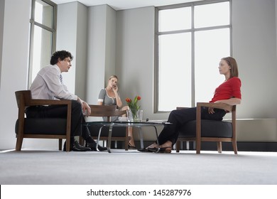 Three Businesspeople Sitting At Office Table And Talking