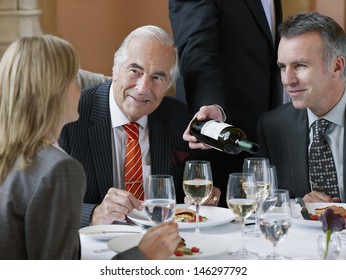 Three businesspeople talking at restaurant table as waiter serves wine