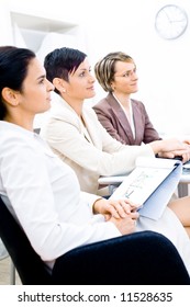 Three businesswoman attending on business training. Sitting in a row, making notes, smiling.