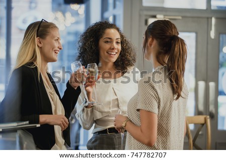 Three businesswomen are enjoying glasses of wine at a bar after work. 