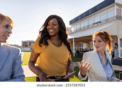 Three businesswomen are standing on a rooftop terrace, enjoying the sunshine and having an informal meeting during their coffee break - Powered by Shutterstock