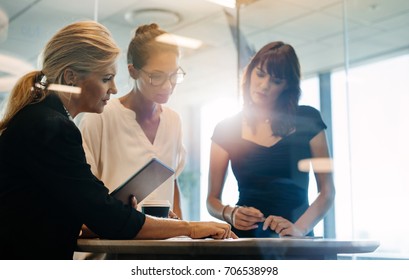 Three businesswomen standing at the table and discussing new projects. Corporate professionals brainstorming over new business ideas.