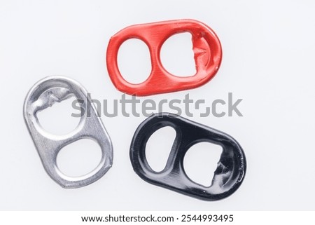 Three can pull tabs, one red, one silver, and one black, are arranged horizontally on a white background.