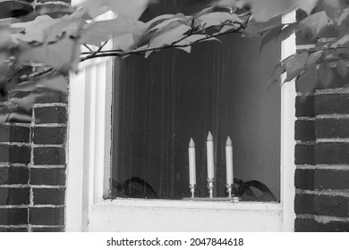 Three candles symbolizing the father, the son and the holy spirit in the window of an old brick church in black and white..