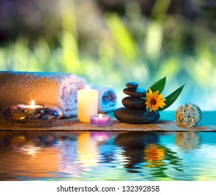 three candles and towels black stones and orange daisy on water