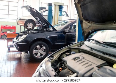 Three Cars In An Automotive Repair Shop Undergoing Maintenance, Repair And Service, One On A Hoist And Two With The Engine Compartments Open