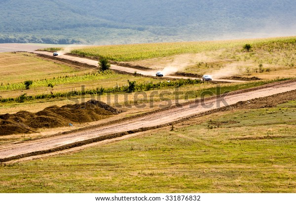 three cars on country dusty roads passing through a\
field planted with corn and other vegetables daylight dust way\
drive line car plant summer nature land rural grass farmland farm\
landscape romania v