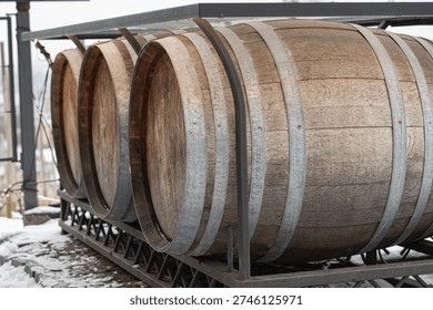 Three casks aligned on ironwork rack, icy perimeter and snowy courtyard, urban warehouse backdrop with vintage patina and textured staves, smallbatch staging for seasonal