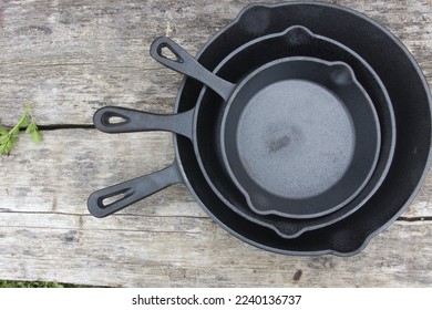 Three cast iron pans placed one inside the other on a wooden table. Cast iron cookware of various sizes used for rustic cuisine cooking.