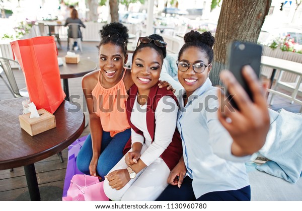 3人のアフリカ系のカジュアルな女の子が 色と買い物袋を持ってアウトドアを歩いています スタイリッシュな黒人女性は 電話で買い物をしたり 自撮りをしたりします の写真素材 今すぐ編集