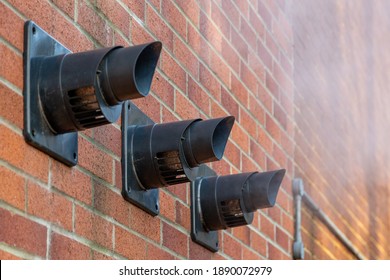 Three central heating boiler flues releasing steam on the exterior of a brick house