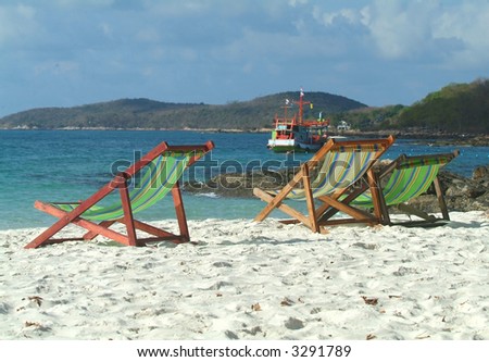 Three chairs on the beach with a small, wooden passenger ferry in the background. Koh Samet, Rayong province, Thailand.