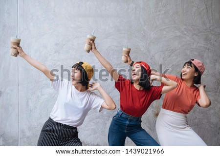 Three cheerful asian female teenager friends with pearl milk tea cup laughing together against grey concrete background