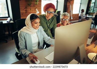 Three cheerful businesswomen having a discussion while looking at a computer screen in an office. Multicultural businesswomen working as a team in a modern co-working office. - Powered by Shutterstock