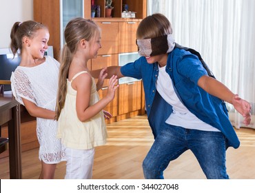 Three cheerful children playing with blindfold and laughing at home interior
