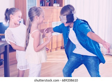 Three cheerful children playing with blindfold and laughing at home interior