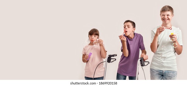 Three cheerful disabled children with Down syndrome and cerebral palsy smiling while blowing soap bubbles, standing together isolated over white background. Lifestyle of special children concept