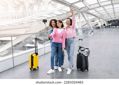 Three Cheerful Female Friends Taking Photo With Selfie Stick At Airport, Group Of Happy Young Women Travelling Together, Posing At Smartphone Camera While Standing With Luggage At Terminal Hall - Powered by Shutterstock