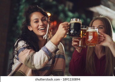 Three cheerful girlfriends are having fun time in pub. They are toasting. Friendship concept.