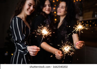 Three cheerful girls in a festive mood holding sparklers in a dark room. Sparks flying in different directions. - Powered by Shutterstock